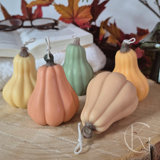 Handgemaakte pompoenkaarsen in warme herfstkleuren, gezellige decoratie op tafel met herfstbladeren.