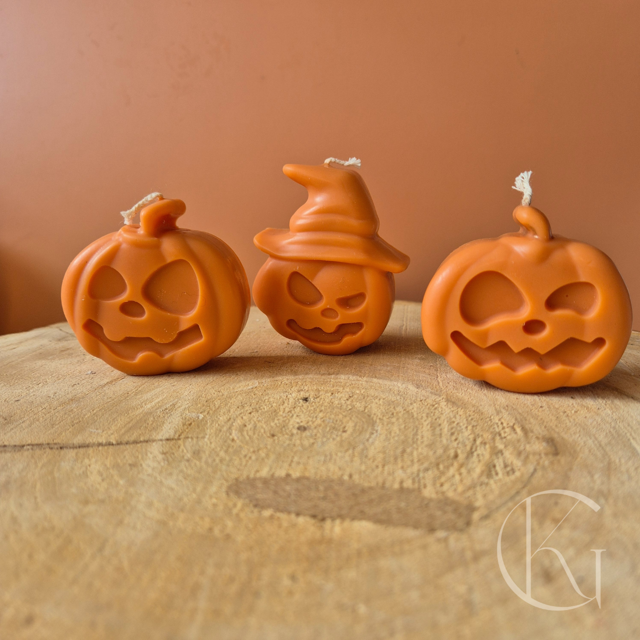 Drie handgemaakte pompoenkaarsen met verschillende gezichtjes in warme oranje tint, vrolijke en spooky Halloween decoratie van duurzame, geurloze sojawas.