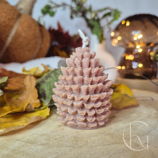 Kleine lichtbruine dennenappelkaars, sfeervol gecombineerd met herfstbladeren en houten schaal