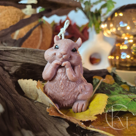 Handgemaakte bruine eekhoornkaars met zwarte oogjes, sfeervol op de herfsttafel met hout en bladeren als bosdecoratie.